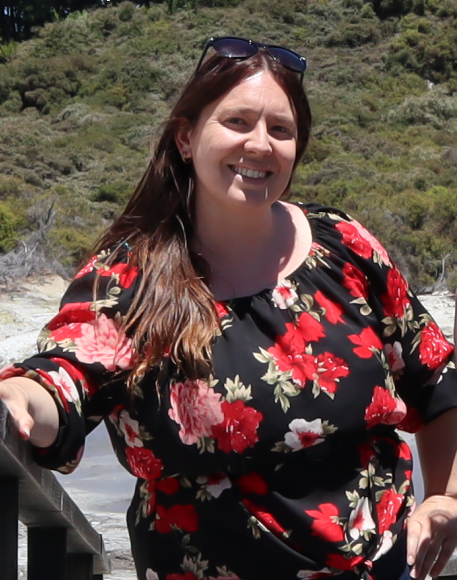 A smiling Katie Haggath, TechCommNZ President, standing on steps at a beach